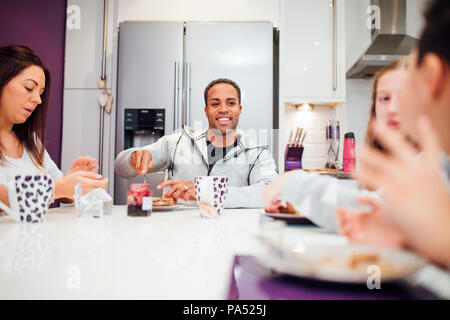 Familie von vier sind, genießen Sie das Frühstück gemeinsam zu Hause. Sie sind alle lachen, während sie Toast und Marmelade. Stockfoto