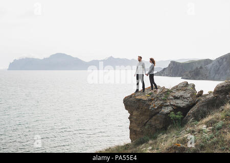 Junges Paar Nordic Walking am Meer mit Blick auf die Berge im Frühling, lässigen Stil Bekleidung Pullover und Jeans Stockfoto