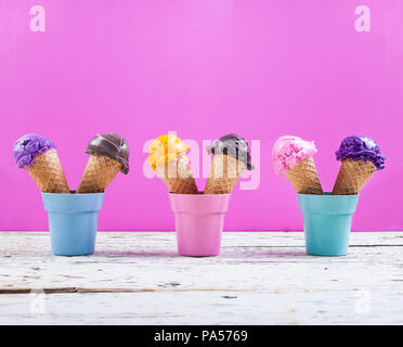 Verschiedene Eisportionierer auf fuchsia Hintergrund mit sortierten Kugeln der Blaubeere, Schokolade, Erdbeere, Orange, Eis, Waffeln Stockfoto