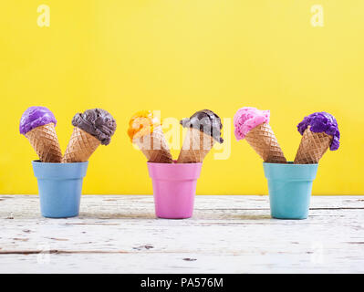 Verschiedene Eisportionierer auf gelbem Hintergrund mit sortierten Kugeln der Blaubeere, Schokolade, Erdbeere, Orange, Eis, Waffeln Stockfoto
