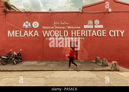 Malacca, Melaka, Malaysia - Dec 15, 2017: Frau zu Fuß durch die Seitenwand der typischen roten Gebäude im Kolonialstil im Zentrum von Melaka. Die Stadt ist von der Unesco Stockfoto