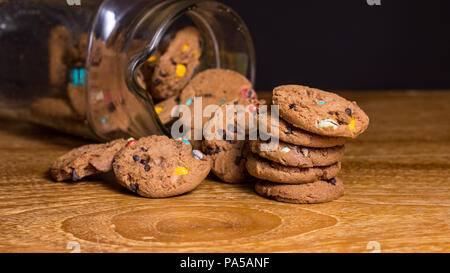 Choc Chip Cookies smartie Fallen aus Glas auf Holz- Tisch. Stockfoto