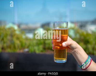 Hand mit Glas Bier an einem sonnigen Tag im festlichen Rahmen Stockfoto