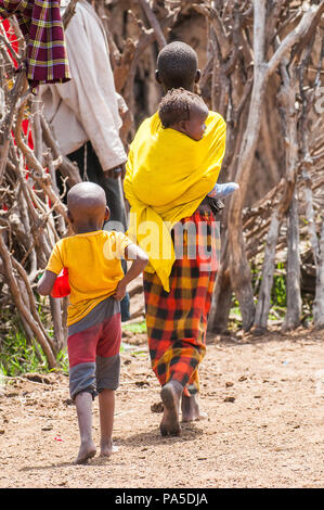 AMBOSELI, Kenia - 10. OKTOBER 2009: Unbekannter Massai Frau trägt ihr Baby auf dem Rücken tragen Tribal typische Kleidung in Kenia, Oct 10, 2009. Masse Stockfoto