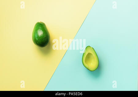 Avocado in Scheiben geschnitten mit Saatgut, ganze Früchte auf blauem und gelbem Hintergrund. Ansicht von oben. Pop Art Design, kreative Sommer essen Konzept. Minimale flach Stil Stockfoto