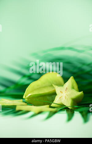 Exotische Star Fruit oder averrhoa carambola über tropical Green Palm Blätter auf Türkisfarbenem Hintergrund. Kopieren Sie Platz. Pop Art Design, kreative Sommer Konzept Stockfoto