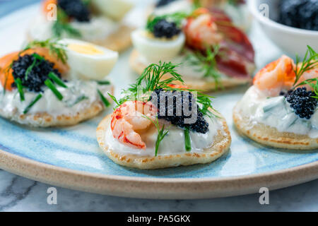 Auswahl an Cocktail Blinis mit Lachs, geräucherter Bresaola, Langusten, Kaviar, Wachteleier und Sauerrahm - gourmet Party Food Stockfoto