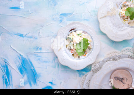 Russische traditionelle New Year's Salat von Gemüse und Fleisch, mit Mayonnaise. In einem Glas serviert und mit Petersilie dekoriert, auf einem weißen Tisch. Stockfoto