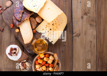 Verschiedene Käse klassische Wahl, auf einer alten Holzplatte, Nüsse, Snacks und ein Glas Bier Stockfoto