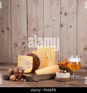 Verschiedene Käse klassische Wahl, auf einer alten Holzplatte, Muttern und ein Glas Bier Stockfoto