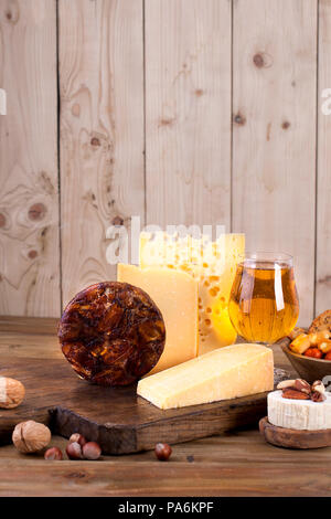 Verschiedene Käse klassische Wahl, auf einer alten Holzplatte, Nüsse, Snacks und ein Glas Bier Stockfoto