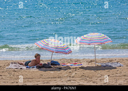 Bournemouth, Dorset, Großbritannien. Juli 2018 21. UK Wetter: heiß und sonnig in Bournemouth Strände, als Sonnenanbeter Kopf an der Küste der Sonne zu Beginn der Sommerferien zu tränken. Junger Mann, jugendlich Sonnenbaden am Strand unter Sonnenschirmen. Credit: Carolyn Jenkins/Alamy leben Nachrichten Stockfoto