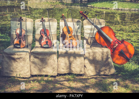 Musik und Natur Konzept. Saiteninstrumente, ein Cello und drei Violinen auf der zeremoniellen Stühle in der Natur. Close Up. Stockfoto