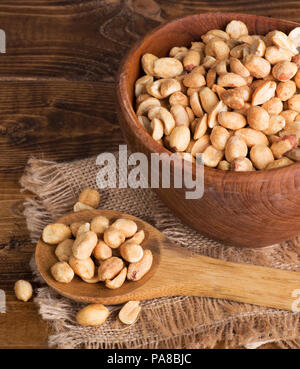 Trocken geröstete Erdnüsse in eine hölzerne Schüssel und Löffel auf eine Leinwand, Stoff und Holz Oberfläche Stockfoto