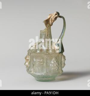 Glaskanne. Kultur: Roman. Abmessungen: H.: 3 3/4 x 2 1/2 x 1 1/8 in. (9,5 x 6,4 x 2,9 cm). Datum: 1. Halbjahr 1. Jh. N.CHR.. Translucent Hellblau grün, mit der gleichen Farbe. Auch rim, Heruntergeklappt, rund, und in; abfackeln Mund; hohe Hals nach unten erweitern, abfallende, leicht konvex Schulter, gedrungenen Körper mit sechseckigen Seiten; Niedrig mit flachem Boden; gegabelten Griff an Schulter, erarbeitet und in eine Kurve, dann drehte er sich in Horizontal und schleppte am Rand der Felge und der Oberseite der Hals in mehreren Falten. Dekoration in der Entlastung in drei Registern: auf die Schulter, sechs Bögen, jede con Stockfoto