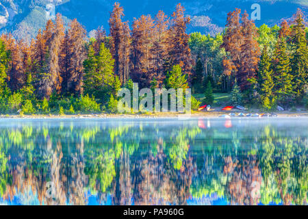 Bunten Bäumen am Ufer des Patricia Lake, Jasper National Park, Kanada. Das ruhige Wasser spiegeln die Bäume und ein paar Kanus auf dem Wasser ed Stockfoto