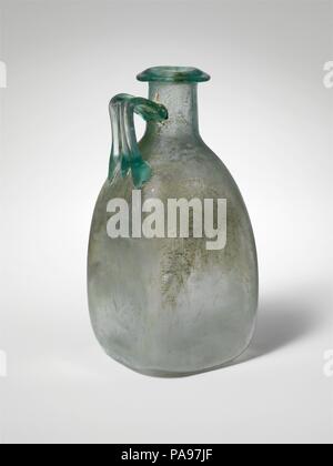 Glaskanne. Kultur: Roman. Abmessungen: Andere: 5 3/4 x 2 5/8 in. (14,6 × 6,7 cm). Datum: 1.-2. Jh. N.CHR.. Transluzent blau grün, mit der gleichen Farbe. Rim ausgeklappt, unten, oben und in den Mund, mit der abgeschrägten Oberfläche; zylindrische Hals, leicht nach unten erweitert, mit leichten Schnittspuren um die Basis; schräge Schulter mit abgerundeten Ecken; quadratische Körper mit leicht konkaven Seiten; ungleichmäßige, konkav unten; Strap Griff mit drei Rippen, auf der Schulter, senkrecht nach oben gezeichnet, dann gebogen und ab und an den Hals mit Rückwärts über Trail befestigt. Intakt, außer einem sm Stockfoto