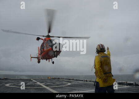 Ein besatzungsmitglied an Bord der Coast Guard Cutter Stratton (WMSL 752) leitet die Einführung eines eingeschifft MH-65 Dolphin helicopter Crew in der Nähe der Beringstraße, 10. Juli 2018. Die stratton Crew patrouillieren oberhalb des Polarkreises zur Unterstützung der Operation Arktis Shield 2018. Coast Guard Foto von Leutnant Brian Dykens. Stockfoto