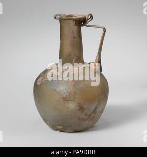 Glaskanne. Kultur: Roman. Abmessungen: 4 1/8 in. (10,5 cm) Andere: 2 3/4 in. (7 cm) Durchm. Von rim: 1 1/8 in. (2,8 cm). Datum: 2.-3.Jh. N.CHR.. Durchsichtig gelb grün; in der gleichen Farbe. Rim gefaltet ungleichmäßig aus, rund, und in; leicht trichterförmig zylindrische Hals, mit schnittspuren an der Basis; kugelförmigen Körper; konkave Unterseite; Strap Griff in drei Dicken kralle Pads an Schulter, erarbeitet und in horizontal gedreht, mit einem doppelten vertikalen als Daumen oben rim Falten, und dann brach auf von Hals- und Außenrand der Felge nach oben. Intakt; viele Blasen; Mattierung, Lochfraß, und ich Stockfoto