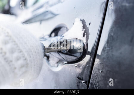 Junge schöne Frau in ziemlich weiß Gestrickte Handschuhe versuchen, das Fahrzeug an einem Wintermorgen zu öffnen. Nahaufnahme eines Schlüssel in das Schloss von gefrorenen Auto eingefügt Stockfoto