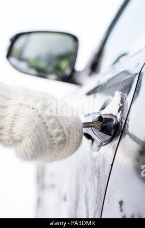 Junge hübsche Dame in Hipster weiß Gestrickte Handschuhe versuchen, das Fahrzeug an einem Wintermorgen zu öffnen. Nahaufnahme eines Schlüssel in das Schloss von gefrorenen Auto eingefügt Stockfoto