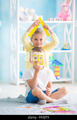 Ein kleines Mädchen mit ein Junge sitzt auf dem Boden und halten ein farbiges Papier Stockfoto