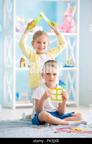 Ein kleines Mädchen mit ein Junge sitzt auf dem Boden und halten ein farbiges Papier Stockfoto