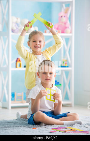 Ein kleines Mädchen mit ein Junge sitzt auf dem Boden und halten ein farbiges Papier Stockfoto