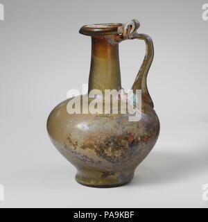 Glaskanne. Kultur: Roman. Abmessungen: 4 5/16 in. (11 cm) Andere: 3. 7,6 cm (3 Zoll) Durchm. Von rim: 1 5/16 in. (3.3 cm) Durchm. Der Fuß: 1 9/16-in. (3,9 cm). Datum: 1. Jh. N.CHR.. Kleine ein- Kanne Translucent gelb grün; in gleicher Farbe. Rim ausgeklappt, unten, rund, und oben, mit abgeschrägter äußerer Kante über dem Abfackeln Mund, leicht konisch zylindrischer Hals, mit schnittspuren an der Basis; Hocke, bauchigen Körper, in geschwungenen, integral, hohen Basis ring; konkave Unterseite; Strap Griff in zwei breiten Klauen an der vorderen und an der dreieckigen Pad an der Rückseite Ausbreitung auf der Unterseite des Stutzens mit Werkzeug zu Schulter Stockfoto
