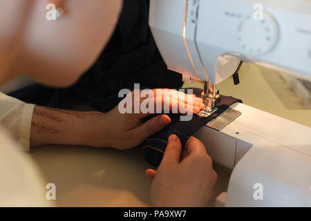 Frau arbeitet mit Nähmaschine.  Schwarzem Stoff und Hände. Atelier oder Design-Studio auf Schneiderei. Nahaufnahme. Stockfoto