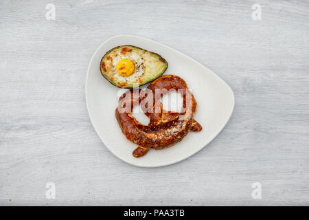 Eier gebacken in Avocado auf Platte mit Brezel Stockfoto