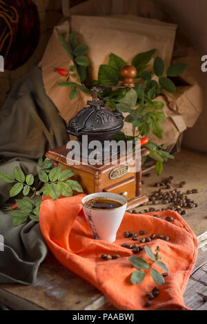 Tasse Kaffee, eine kaffeemühle unter den grünen Blättern. Vintage Style. Stockfoto