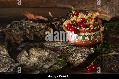Die Beeren in ein Ton Cup stand in der birkenrinde vor dem Hintergrund des Boards. Tageslicht, close-up. Stockfoto