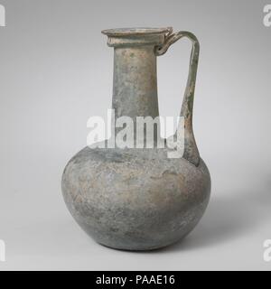 Glaskanne. Kultur: Roman. Abmessungen: H.: 5 3/4 in. (14,5 cm) Durchm.: 4 1/16-in. (10,3 cm) Durchm. Von rim: 1 13/16-in. (4,6 cm). Datum: Mitte 1.-2. Jh. N.CHR.. Transluzent blau grün; in gleicher Farbe. Kragen rim ausgeklappt, unten, oben, und heraus, mit horizontalen äußere Lippe; leicht trichterförmig zylindrische Hals, mit leichten tooling Gedankenstrich um Base; Hocke, kugelförmigen Körper; konkave Unterseite; Strap Griff in zwei große Klaue Pads an den Seiten und kleinere zentralen Rippe, Schulter, erarbeitet und sie sich dann und unten gedreht, gezogenen auf der Hals nach oben und die Felge mit Ende an der oberen Kante der äußeren Dichtlippe Stockfoto