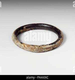 Glas Armband. Kultur: Roman. Abmessungen: H.: 1/2 in. (1,3 cm) Durchm.: 3. 7,6 cm (3 Zoll). Datum: Ca. 2.-4.Jh. N.CHR.. Transluzente sehr dunkel Grün, erscheint schwarz. Kreisförmige Band; runde in Abschnitt aber mit Nut um innere Seite; in quadratischen Abschnitt an der Nahtstelle, wo die Enden der Stange mit unregelmäßigen Schnittspuren gedrückt wurden abgeflacht; kleine pontil Narbe am äußeren Rand der gegenüberliegenden Seite. Intakt; längliche blasen; Mattierung, schwachen Schillern und Patches von dicken, cremigen Verwitterung. Museum: Metropolitan Museum of Art, New York, USA. Stockfoto