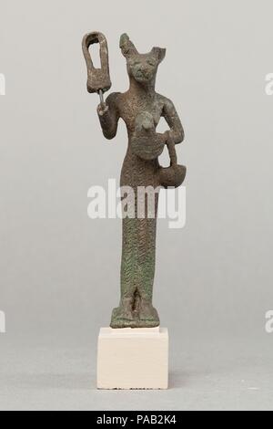 Bastet holding Sistrum. Abmessungen: H 9,7 cm (3 13/16 in.); W. 3,8 cm (1 1/2 in.); D.2.7 cm (1 1/16 in.). Datum: 664-30 v. Chr.. Bastet, hier gezeigt wie eine Katze Göttin, war ein mächtiger Schutz Figur, die auch für ihre Fruchtbarkeit bekannt war. Sie konnte mit einem löwenkopf als gut vertreten werden, sondern als eine Katze Göttin ihren friedlichen Merkmale hervorgehoben wurden. Ihre persönlichen Verzierungen und Kleider sind näher auf Statuetten, oft mehr als andere Göttinnen, und sie führt in der Regel zahlreiche Attribute. Diese Ersatzteile und schlanke Figur hält einen Korb in der Armbeuge den Ellenbogen, eine schützende aegis Aga Stockfoto