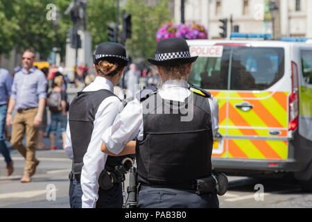 London, England, UK; 13. Juli 2018; Rückansicht von zwei weiblichen Metropolitan Police Officers in der Straße. Unfocused Polizeiwagen hinter Stockfoto