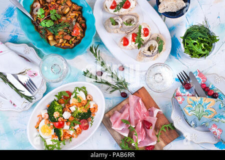 Weißer Tisch mit verschiedenen Speisen, Salate und Snacks, Teller und Servietten. Stockfoto