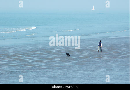 Lady und schwarzer Hund entlang Ost/West Wittering Strand. Diesigen morgen. März. Nasser sand. Stockfoto