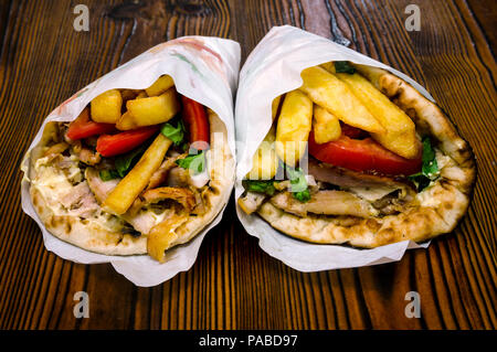 Griechische Pita Gyros (souvlakia), griechische traditionelle Street Food, umwickelt mit weißem Papier umwickeln auf einer hölzernen rustikalen Tisch Stockfoto