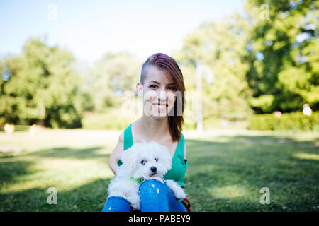 Porträt der schönen Lächeln ungültige junge Frau ohne obere Extremitäten mit ihren kleinen weißen Hund im Park geboren. Stockfoto