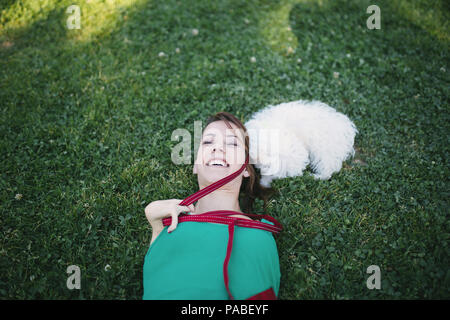 Porträt der schönen Lächeln ungültige junge Frau ohne obere Extremitäten mit ihren kleinen weißen Hund im Park geboren. Stockfoto