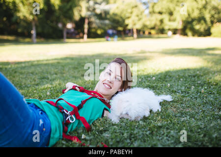 Porträt der schönen Lächeln ungültige junge Frau ohne obere Extremitäten mit ihren kleinen weißen Hund im Park geboren. Stockfoto