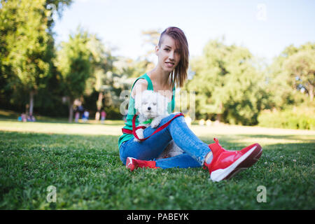 Porträt der schönen Lächeln ungültige junge Frau ohne obere Extremitäten mit ihren kleinen weißen Hund im Park geboren. Stockfoto