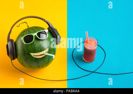 Happy Wassermelone Gesicht Musik hören und Saft im Glas, split Farbe Hintergrund. Stockfoto