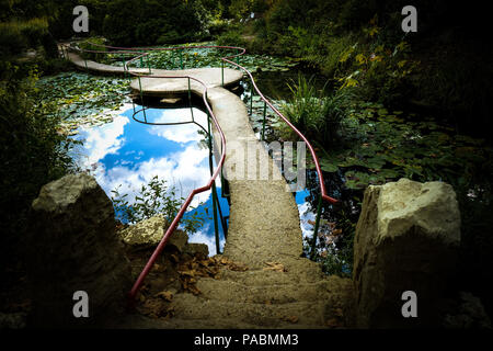 Steinerne Brücke Gasse über einen Teich mit Seerosen und eine Reflexion der Himmel im Wasser Stockfoto