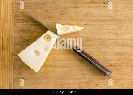 Cut Keil der Niederländischen Maasdamer Käse mit einer kleinen Küche Messer auf einem Bambus Schneidebrett von oben mit Kopie Raum gesehen Stockfoto