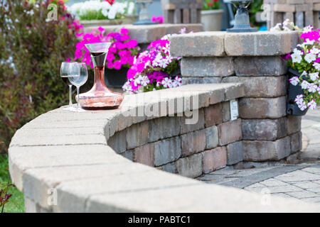 Dekanter Rotwein mit Kohlensäure auf einer gekrümmten Ziegelstein-patio Wand mit zwei weingläser vor bunten Kübelpflanzen Sommerblumen mit Kopie Raum Stockfoto