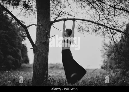 Schwarzweiß-Foto der jungen Frau hangigng auf Zweig des Baumes. Sie will allein sein und Denken ein wenig über das Leben Stockfoto