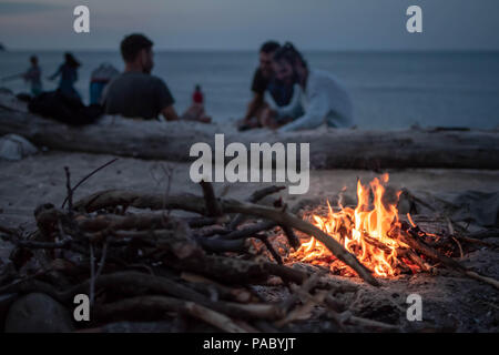 Lagerfeuer am Strand am Meer bei Sonnenuntergang mit einer Gruppe von Freunden im Hintergrund Stockfoto